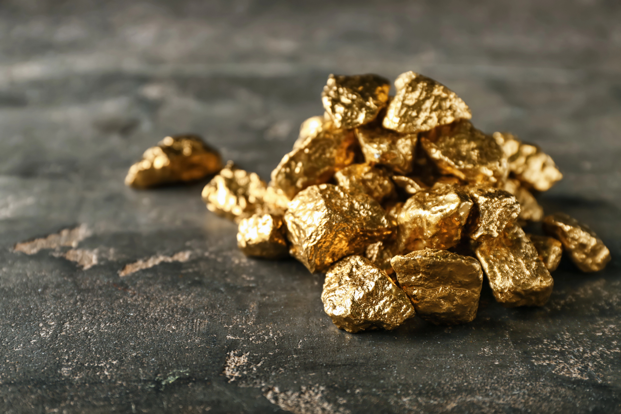 A collection of shiny gold nuggets displayed on a wooden table, showcasing their natural luster and unique shapes.